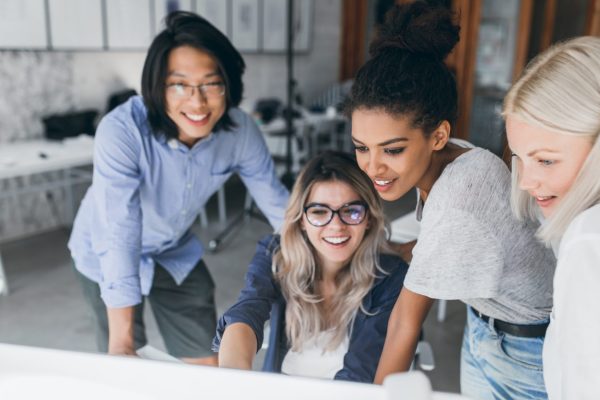 Close-up portrait of freelance it-specialists looking at laptop screen with smile. Asian programmer in glasses helping to mulatto girl in white t-shirt with her project.. Close-up portrait of freelance it-specialists looking at laptop screen with smile. Asian programmer in glasses helping to mulatto girl in white t-shirt with her project.